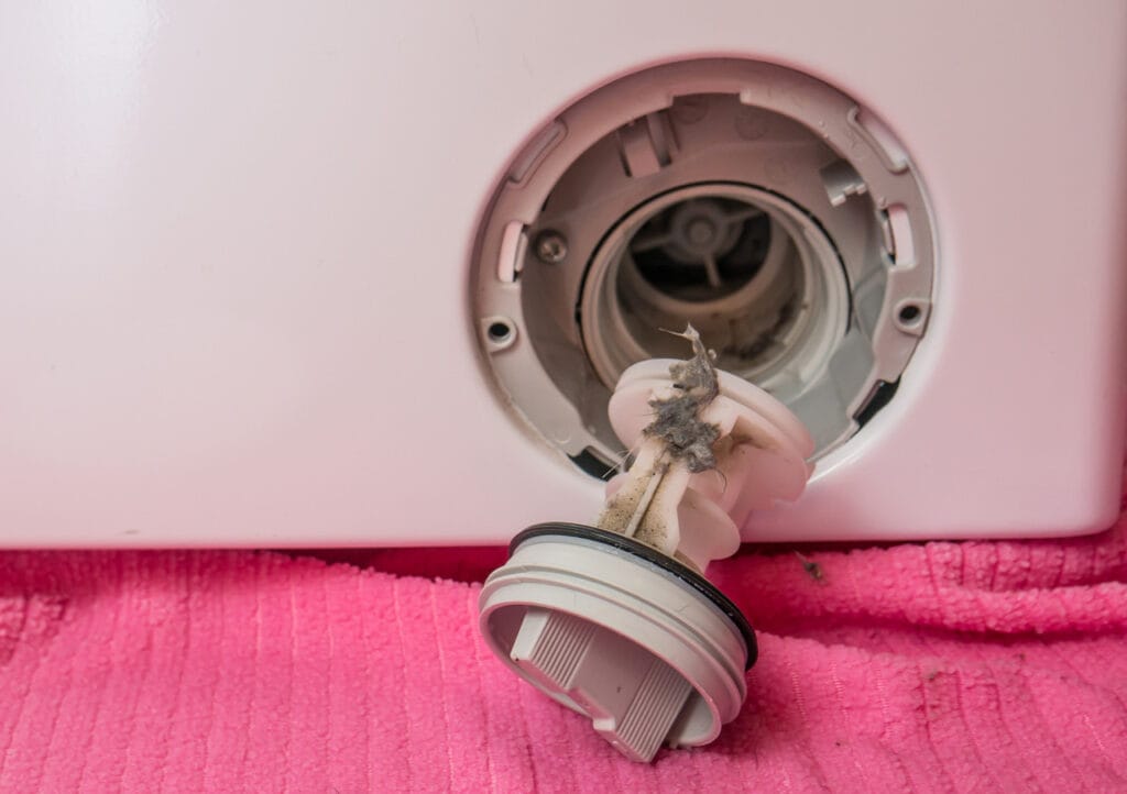 Primo piano della pulizia del filtro della lavatrice, con lo sporco chiaramente visibile