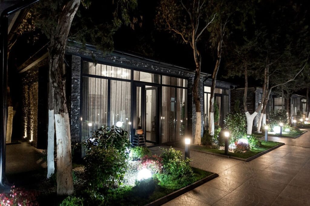 Vialetto illuminato di notte con luci LED da giardino davanti a edifici moderni con ampie vetrate e piante decorative